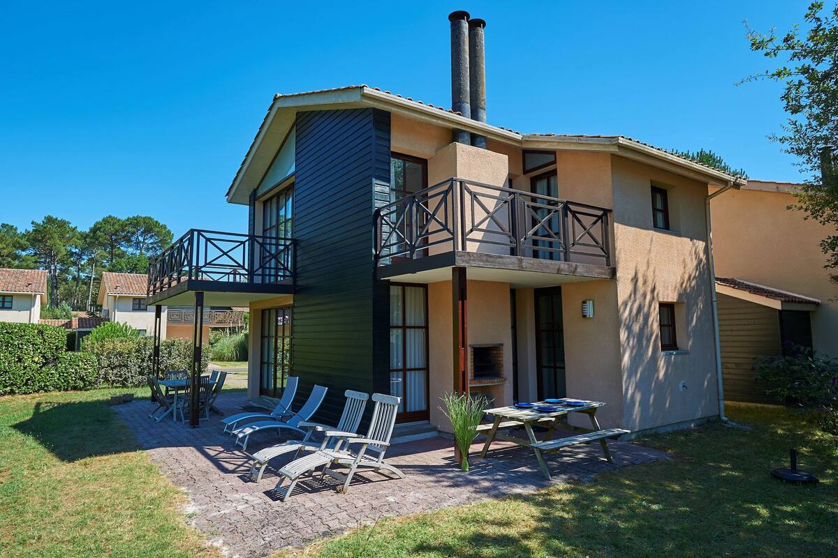 Une maison à deux étages avec un balcon, une terrasse avec des chaises et une table, et une cheminée.