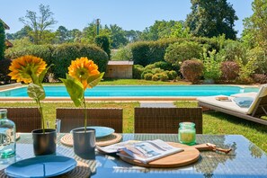 Un cadre agréable au bord de la piscine, avec une table dressée pour deux personnes, une terrasse en bois et une vue sur la piscine.