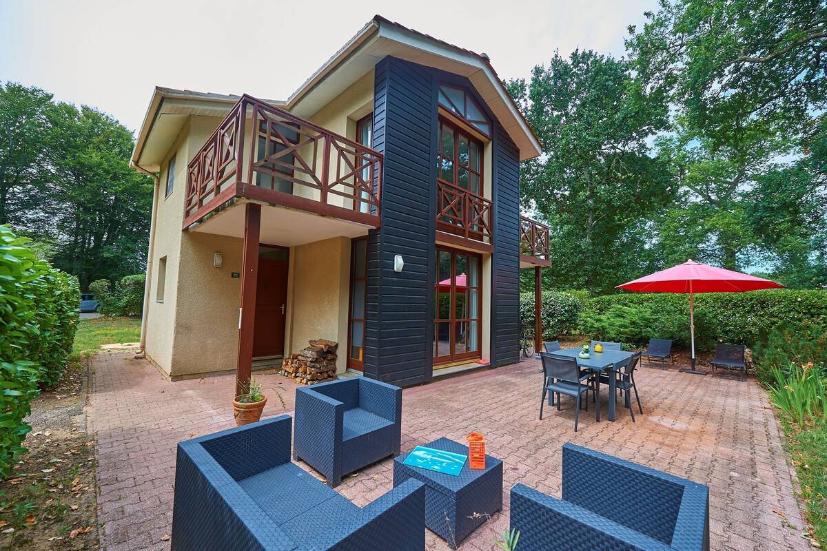 Une maison à deux étages avec un balcon, un espace salon extérieur et un parasol rouge.