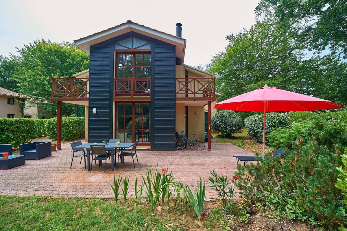 Une maison moderne dotée d’un balcon, d’une terrasse avec mobilier d’extérieur et d’un parasol rouge.
