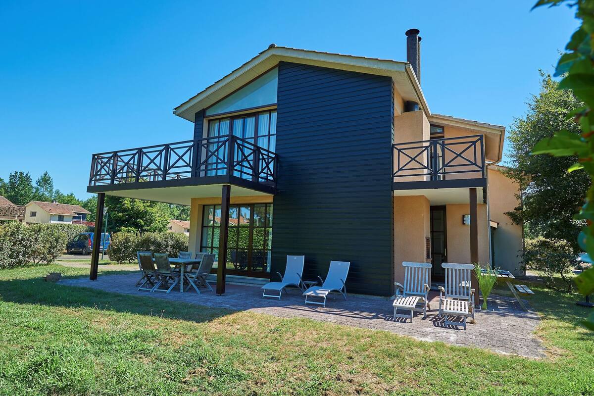 Une maison moderne à deux étages, dotée d’un balcon, d’un espace salon extérieur et offrant une vue dégagée sur les environs.