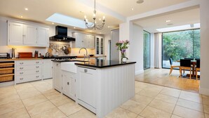 A spacious kitchen with a central island, white cabinetry, and a large window providing a view of the outdoors. - Majestic Oasis, by Veeve (London)