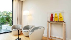 A modern living room with two white armchairs, a small round table, and a glass display case with three colorful figurines. - Majestic Oasis, by Veeve (London)