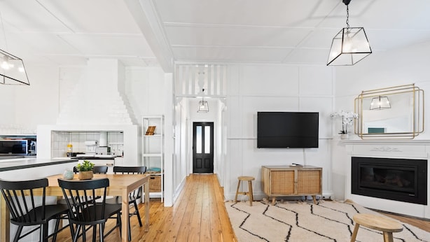 A modern living room with a wooden floor, a TV mounted on the wall, a fireplace, and a dining area with a table and chairs. - Johnno's Cottage - Prime Location - Sleeps 4 (Orange)