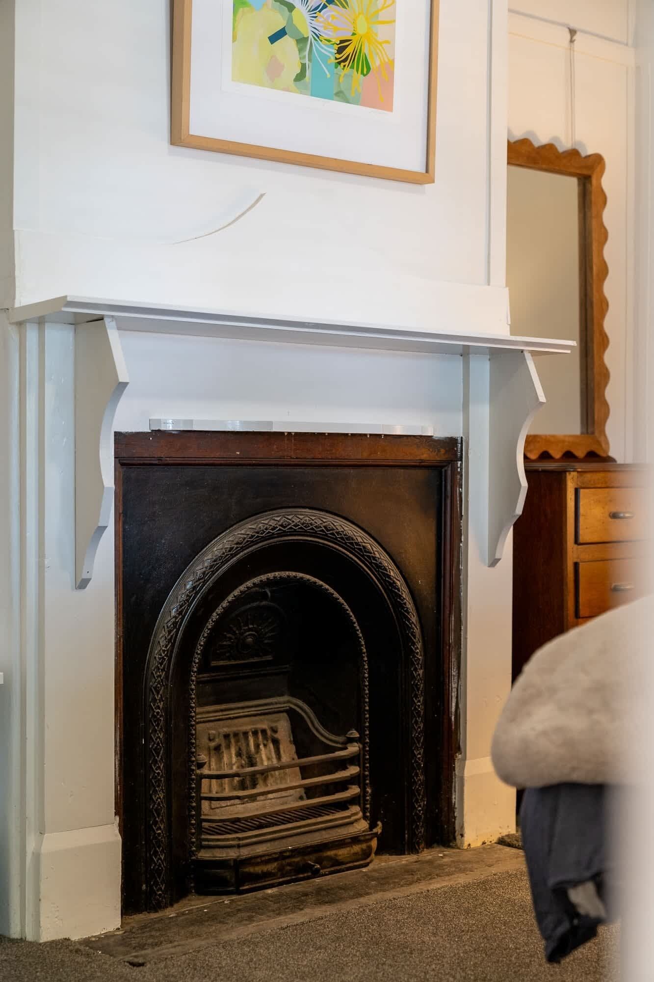 A fireplace with a white mantel, a framed abstract painting above it, and a wooden cabinet to the right.
