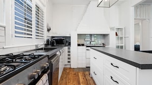 A modern kitchen with white cabinetry, a gas stove, and a microwave. - Johnno's Cottage - Prime Location - Sleeps 4 (Orange)
