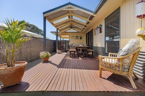 A wooden deck with a covered seating area, potted plants, and a wicker chair.