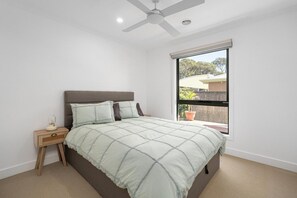 Une chambre à coucher comprenant un lit, une table de chevet, un ventilateur de plafond et une fenêtre donnant sur l’extérieur.