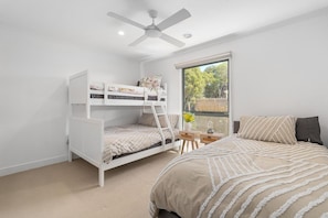 A bedroom with bunk beds, a single bed, a ceiling fan, a window with a view, and a small table with a vase.