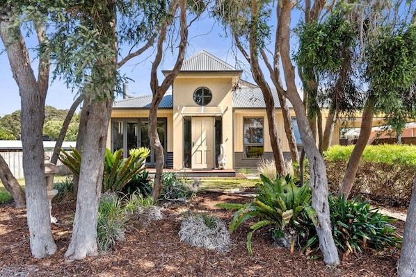 A two-story house with a front porch, surrounded by mature trees and landscaped garden.