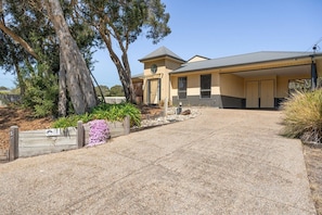 A modern two-story house with a covered porch, a stone pathway leading to the entrance, and a large tree to the left.