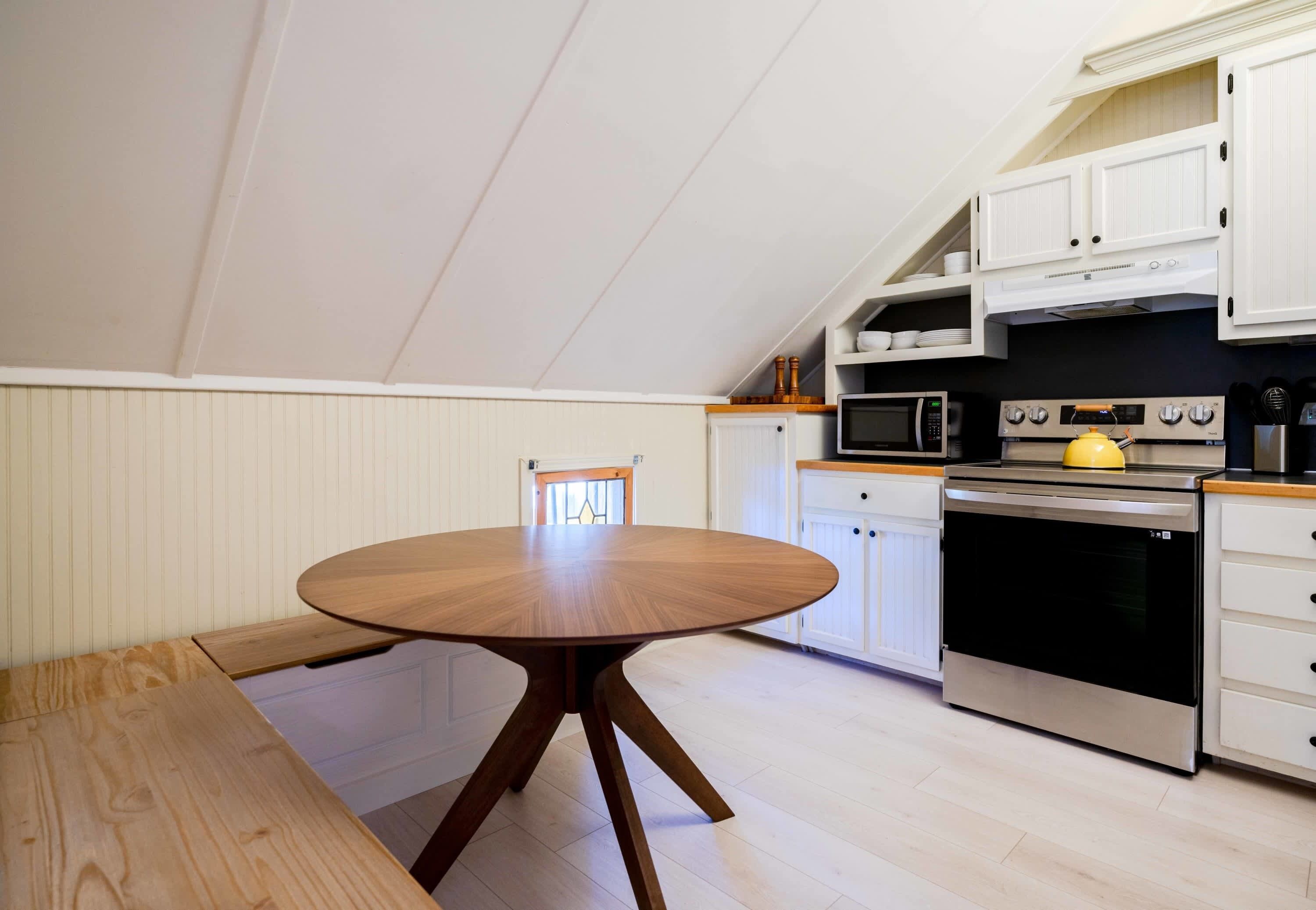 A modern kitchen with white cabinetry, a round wooden table, and a built-in oven.