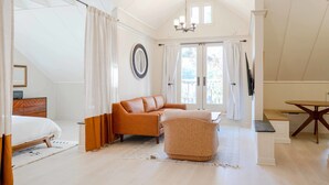 Una habitación amplia con techo alto, un ventanal grande, un sofá, un reposapiés de mimbre y una mesa de comedor.