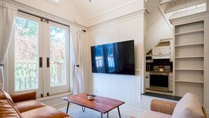 Una sala de estar con un sofá de cuero, una silla de mimbre, una mesa de centro de madera y un televisor de pantalla plana montado en la pared.