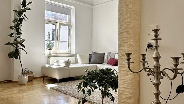 A spacious living room with a white sofa, a large window, and a candelabra. - 90 m2 - Space to Chill & Work & Rest (München)