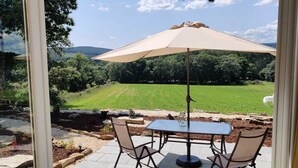 An outdoor patio with a table and chairs, a beige umbrella, and a view of a green field and trees. - La Casita a haven of peace to escape and relax, close to cities and beaches. (Lugo Galicia)