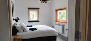 A bedroom with a bed, two windows, a radiator, and a desk. - La Casita a haven of peace to escape and relax, close to cities and beaches. (Lugo Galicia)