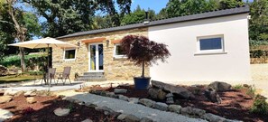 A modern house with a stone exterior, a front porch with chairs, and a potted plant. - La Casita a haven of peace to escape and relax, close to cities and beaches. (Lugo Galicia)