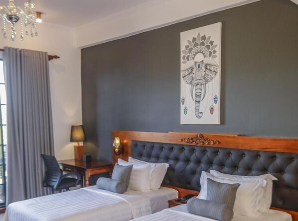 Habitación de hotel con dos camas, un candelabro, un escritorio con lámpara y una gran obra de arte en la pared.