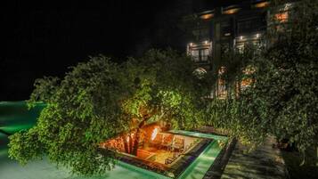 A secluded outdoor area with a pool, surrounded by dense foliage and a building in the background.