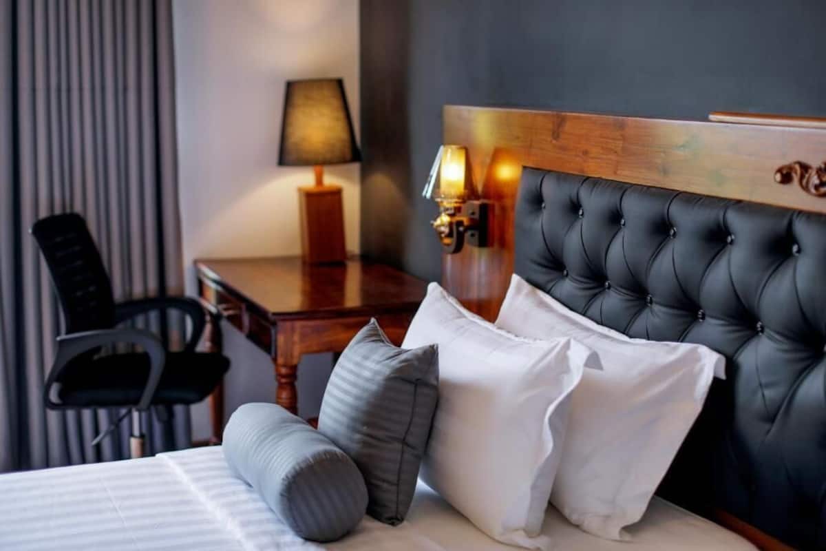 Una habitación de hotel con un cabecero capitonado, un escritorio de madera, una silla y una lámpara.