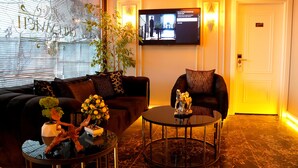 Una sala de estar moderna con un sofá, un sillón y una mesa de centro, con plantas decorativas y un televisor de pantalla plana montado en la pared.