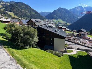 Uma aldeia montanhosa com casas de madeira tradicionais, um edifício moderno com painéis solares e uma vista desobstruída das montanhas ao redor.