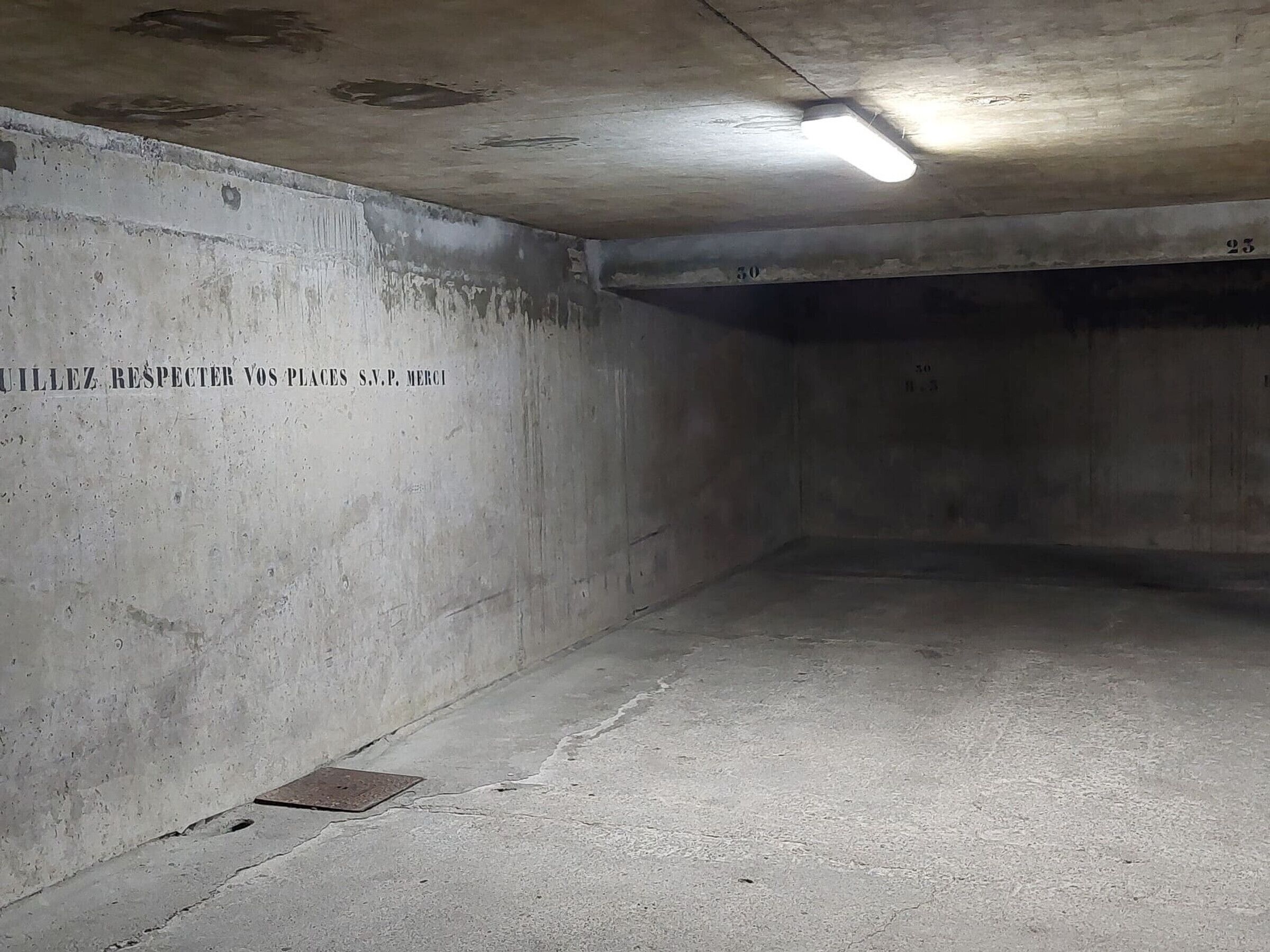 Eine schwach beleuchtete, leere Tiefgarage mit Betonwänden und einer Neonleuchte.