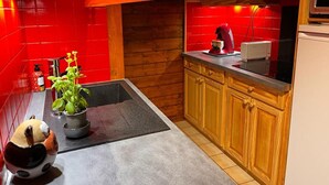 A kitchen with red tiles, wooden cabinets, a black countertop, a red kettle, and a potted plant.