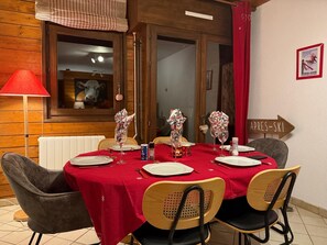 Mesa de jantar posta para quatro pessoas, com toalha vermelha, rodeada por cadeiras de madeira.