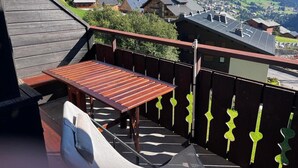 A wooden deck with a table and chairs, overlooking a mountainous village with houses and a clear sky.