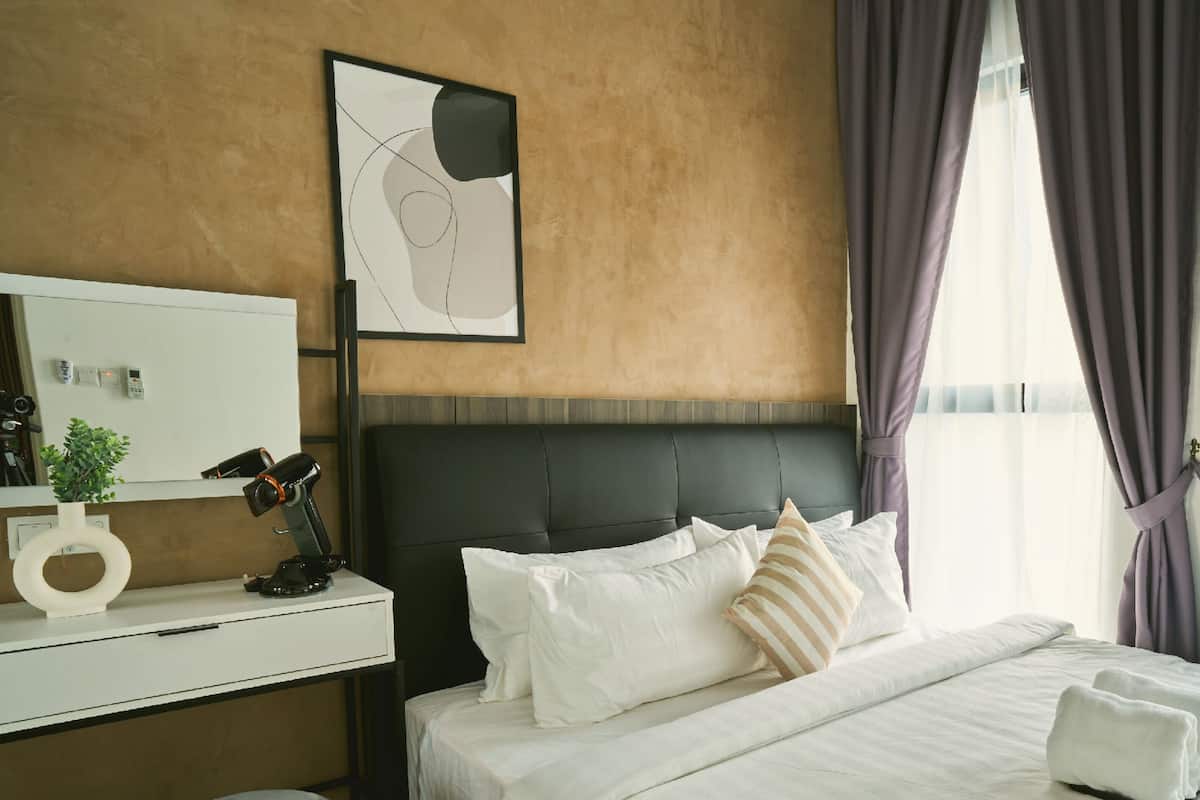 Ein modernes Hotelzimmer mit einem großen Bett, einem Kopfteil, einem Nachttisch mit Lampe, einem gerahmten abstrakten Kunstwerk und einem Fenster mit Vorhängen.