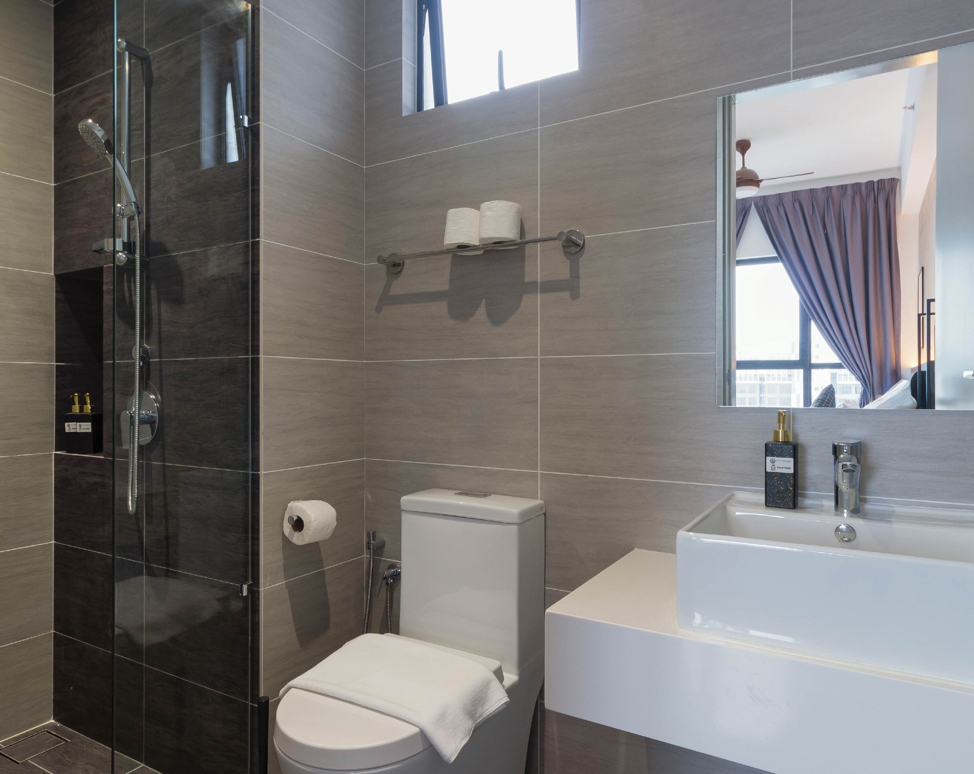 A modern bathroom with a glass-enclosed shower, a white toilet, and a large white sink with a mirror above it.