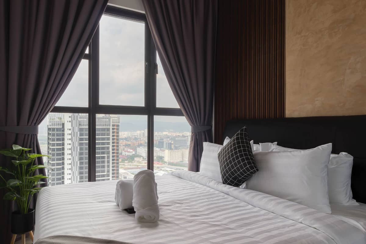 Ein Hotelzimmer mit einem großen Bett, Blick auf die Stadt durch das Fenster und einer Zimmerpflanze.