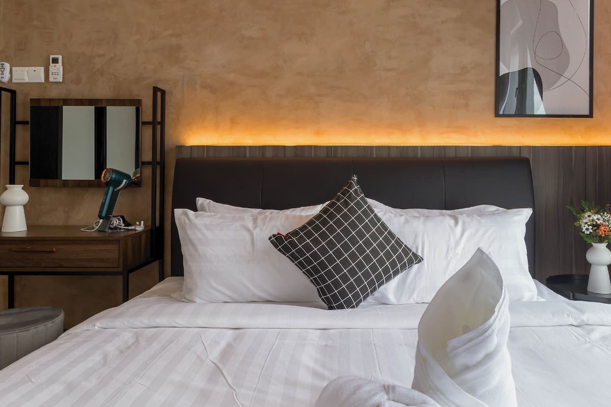 Ein Hotelzimmer mit Bett, Nachttisch mit Lampe, Spiegel und einem gerahmten Kunstwerk an der Wand.