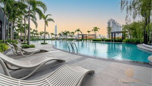 Un espace piscine moderne, avec des chaises longues, des palmiers et une vue sur les gratte-ciel de la ville en arrière-plan.