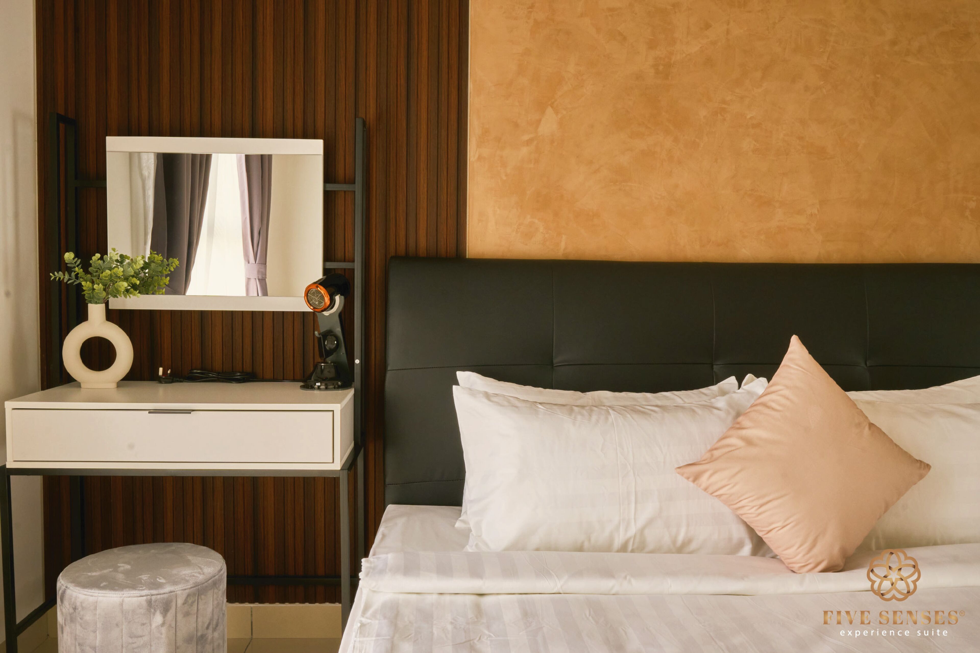 A bedroom with a bed, a bedside table, a mirror, and a small stool.