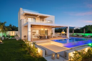 Una casa moderna de dos pisos con piscina, mobiliario exterior y una zona de patio bien iluminada.