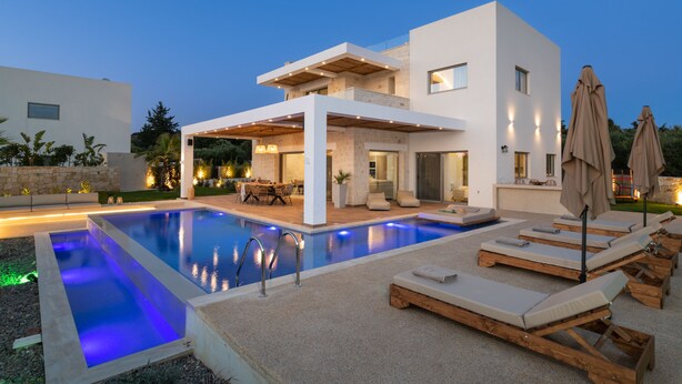 Une maison moderne à deux étages, dotée d’une piscine, d’un espace extérieur aménagé et d’un patio bien éclairé.