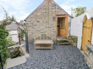 A stone building with a wooden bench in front, a wooden door, and a small stone wall. - The Druids (Corwen)