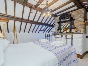 A bedroom with a bed, a stone wall, a wooden ceiling, and a clock. - The Druids (Corwen)