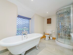 A bathroom with a freestanding bathtub, a toilet, and a shower enclosure with patterned tiles. - The Druids (Corwen)