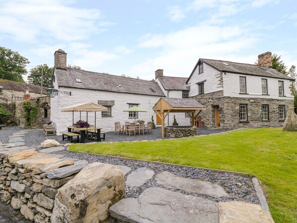 A stone building with a patio area featuring tables and chairs, a wooden pergola, and a stone wall in the foreground. - The Druids (Corwen)