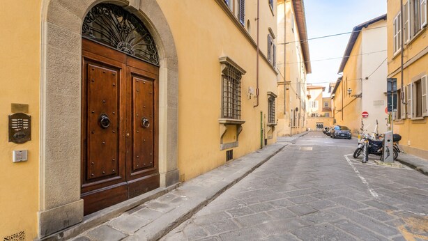 A narrow street with a large wooden double door, stone pavement, and parked cars.