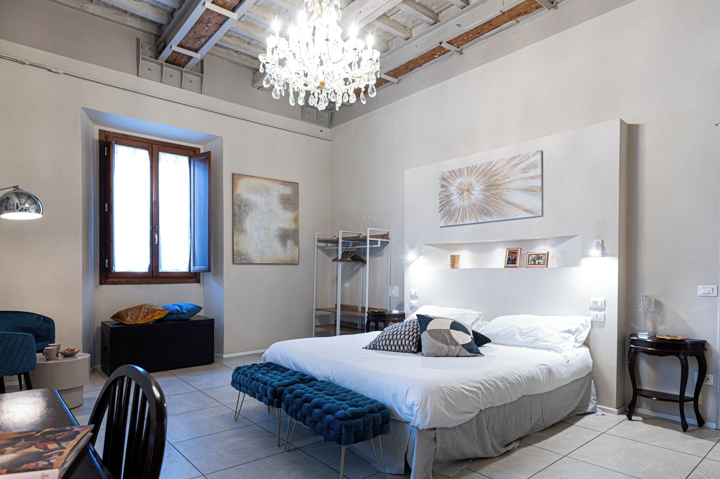 A bedroom with a large bed, a chandelier, a desk, and a chair.
