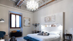 A bedroom with a large bed, a chandelier, a desk, and a chair.