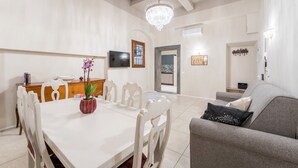 A dining area with a white table and chairs, a chandelier, and a grey sofa with a decorative pillow.