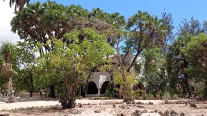 A courtyard with a building featuring an arched entrance, surrounded by various trees and shrubs. - Spacious Villa on Malindi Beach with pool and restaurant next to Golf course (Malindi)