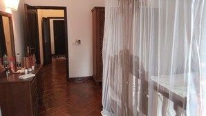 A hotel room with a wooden floor, a bed with a white canopy, a wooden dresser with toiletries, and a mirror. - Spacious Villa on Malindi Beach with pool and restaurant next to Golf course (Malindi)