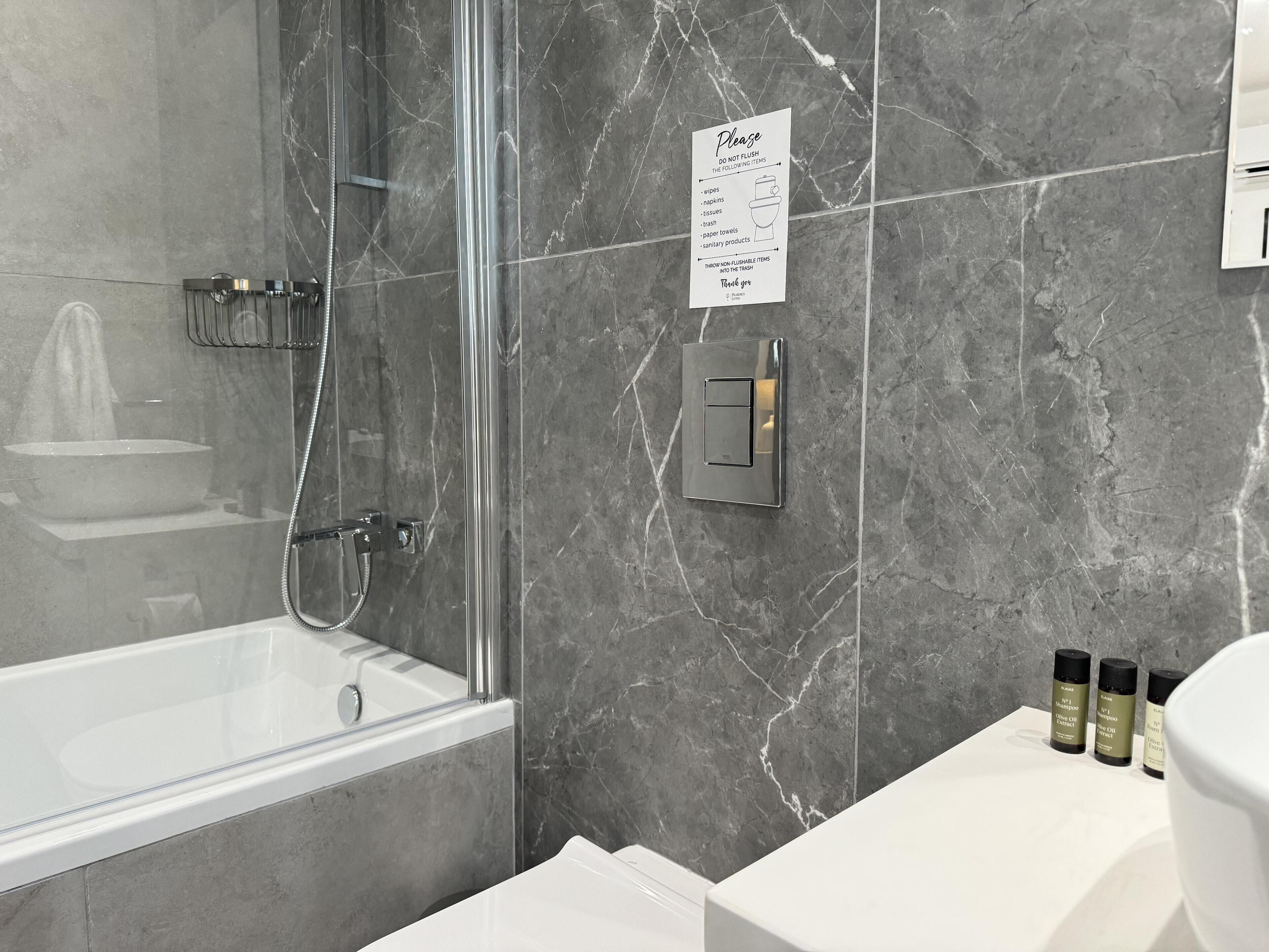 A modern bathroom with a glass-enclosed shower, a white sink, and a marble wall.